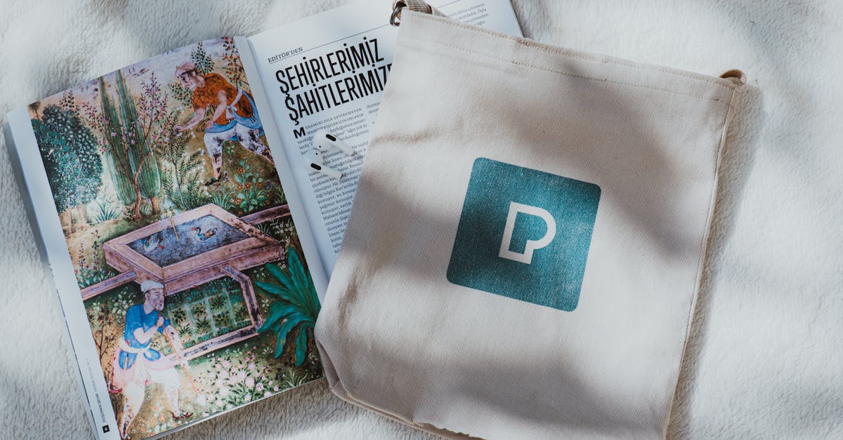 A decorative open book and a tote bag with a logo on a soft textured backdrop.